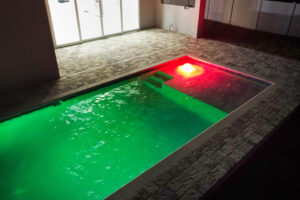 Custom small indoor pool with green tint, stone deck and water feature | Winway Pools