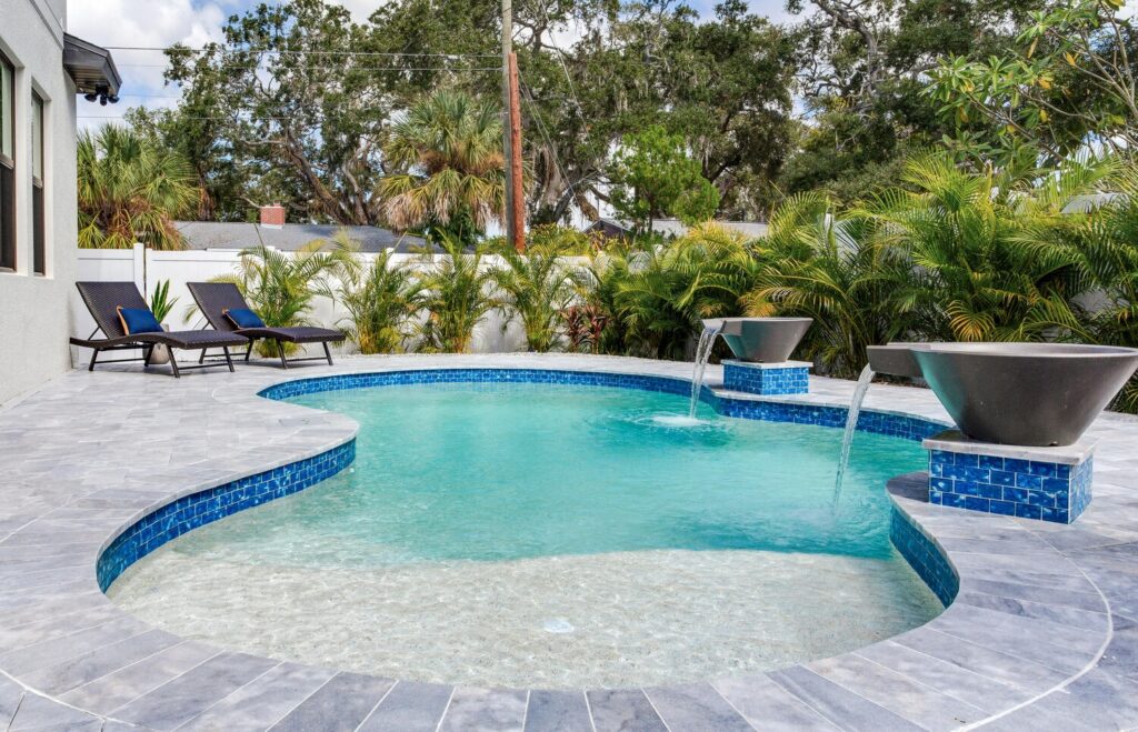 Rectangular swimming pool surrounded by paver decking and mature shade trees
