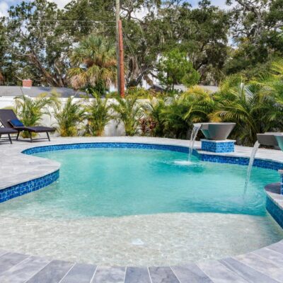 Rectangular swimming pool surrounded by paver decking and mature shade trees