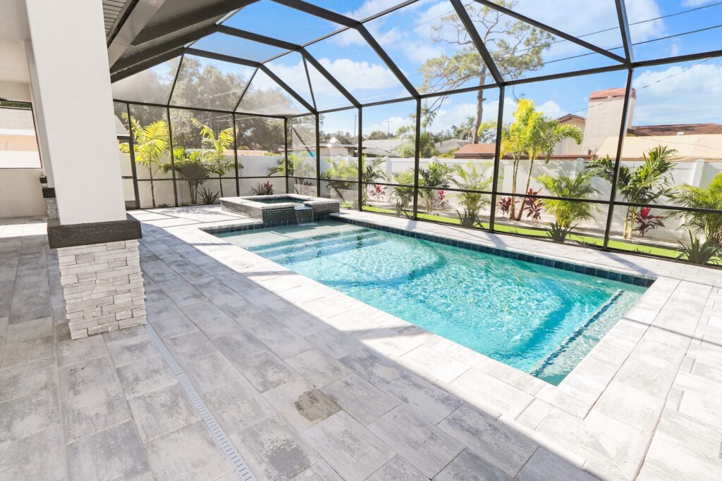 Screen-enclosed swimming pool and raised spa with paver deck and tropical landscaping