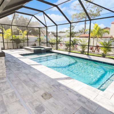 Screen-enclosed swimming pool and raised spa with paver deck and tropical landscaping