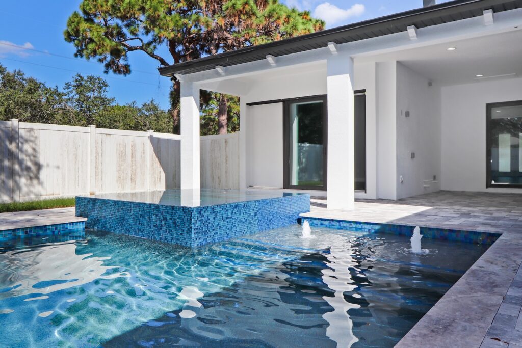 Luxury swimming pool with raised infinity-edge spa and water features beside a custom Florida home